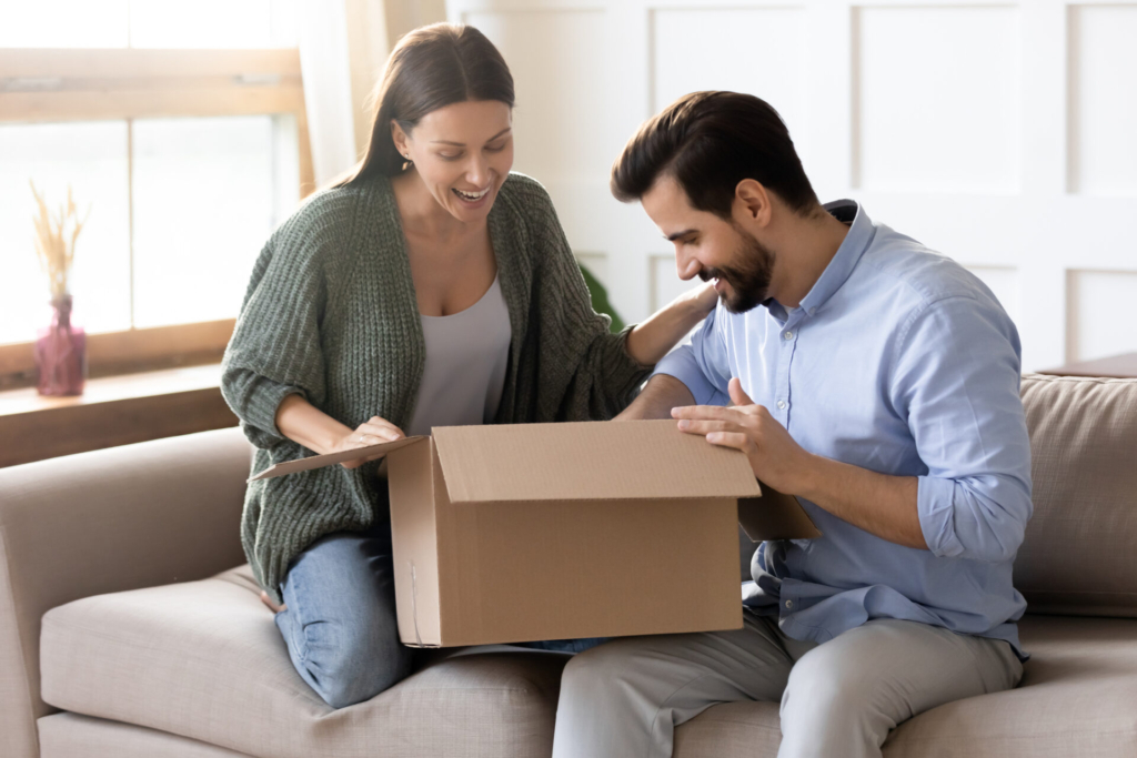 Overjoyed young married couple unpacking cardboard box at home.